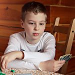 boy holding cards, symbolizing the cards (reasons behind) Outshining AI